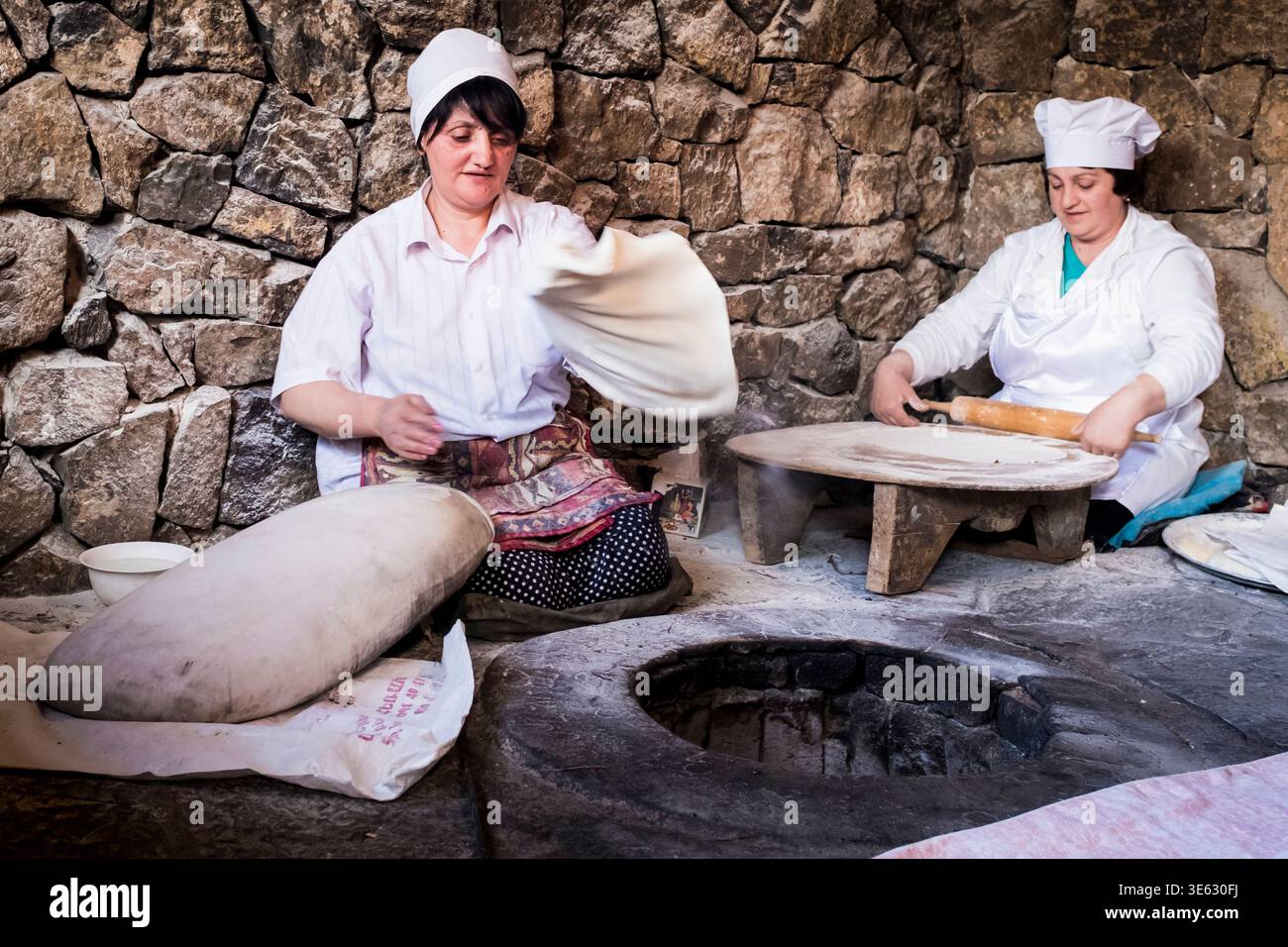 Le donne armene tradizionali preparano il pane nel tandoor, l'impasto rotolato a mano in un autentico ambiente culturale in Armenia. Caucaus, Eurasia. Foto Stock