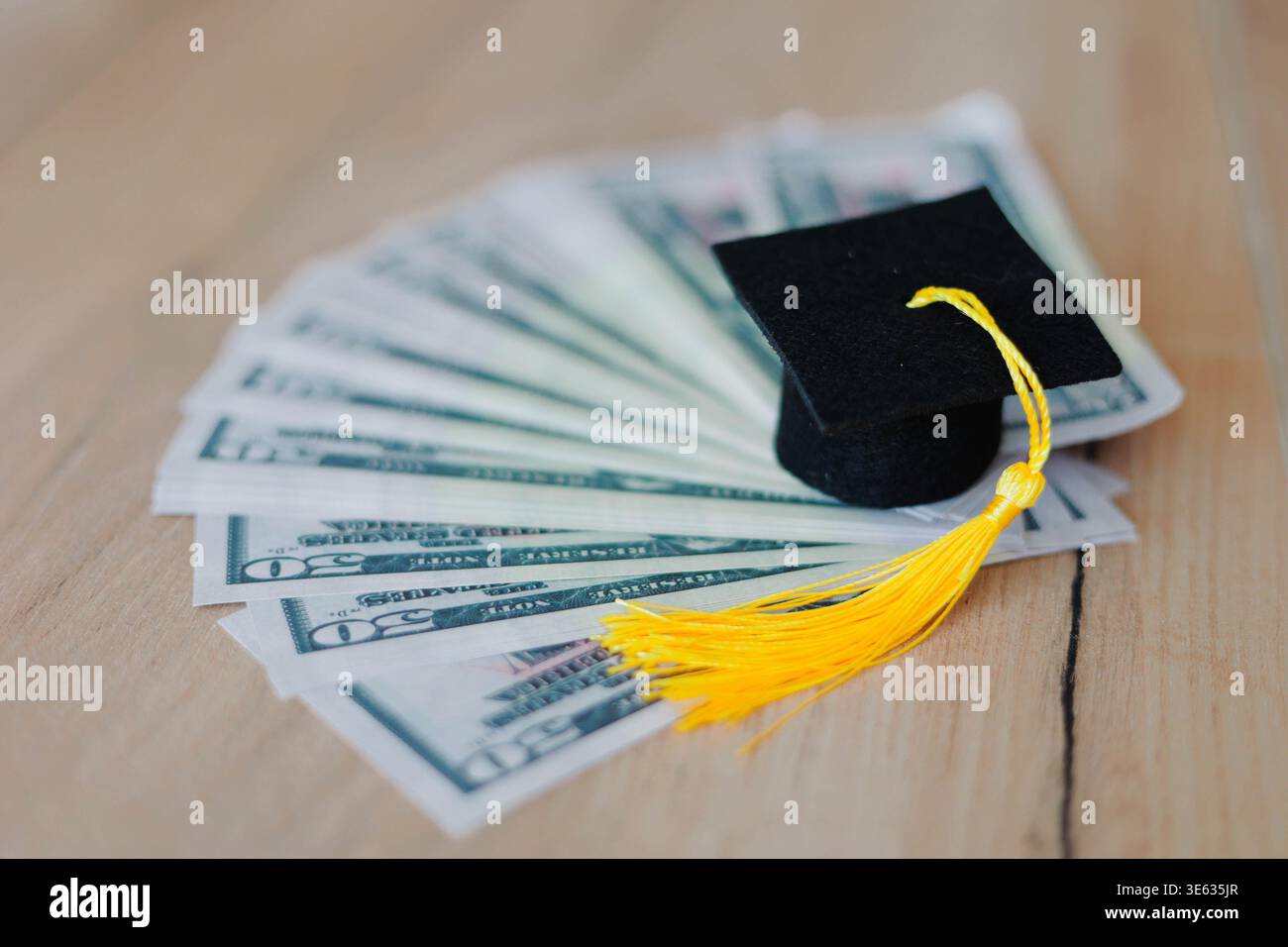 Cappuccio graduato su una pila di banconote da un dollaro su un tavolo di legno. Costo dell'istruzione, tasse scolastiche, debito degli studenti e concetto di investimento finanziario. Foto Stock