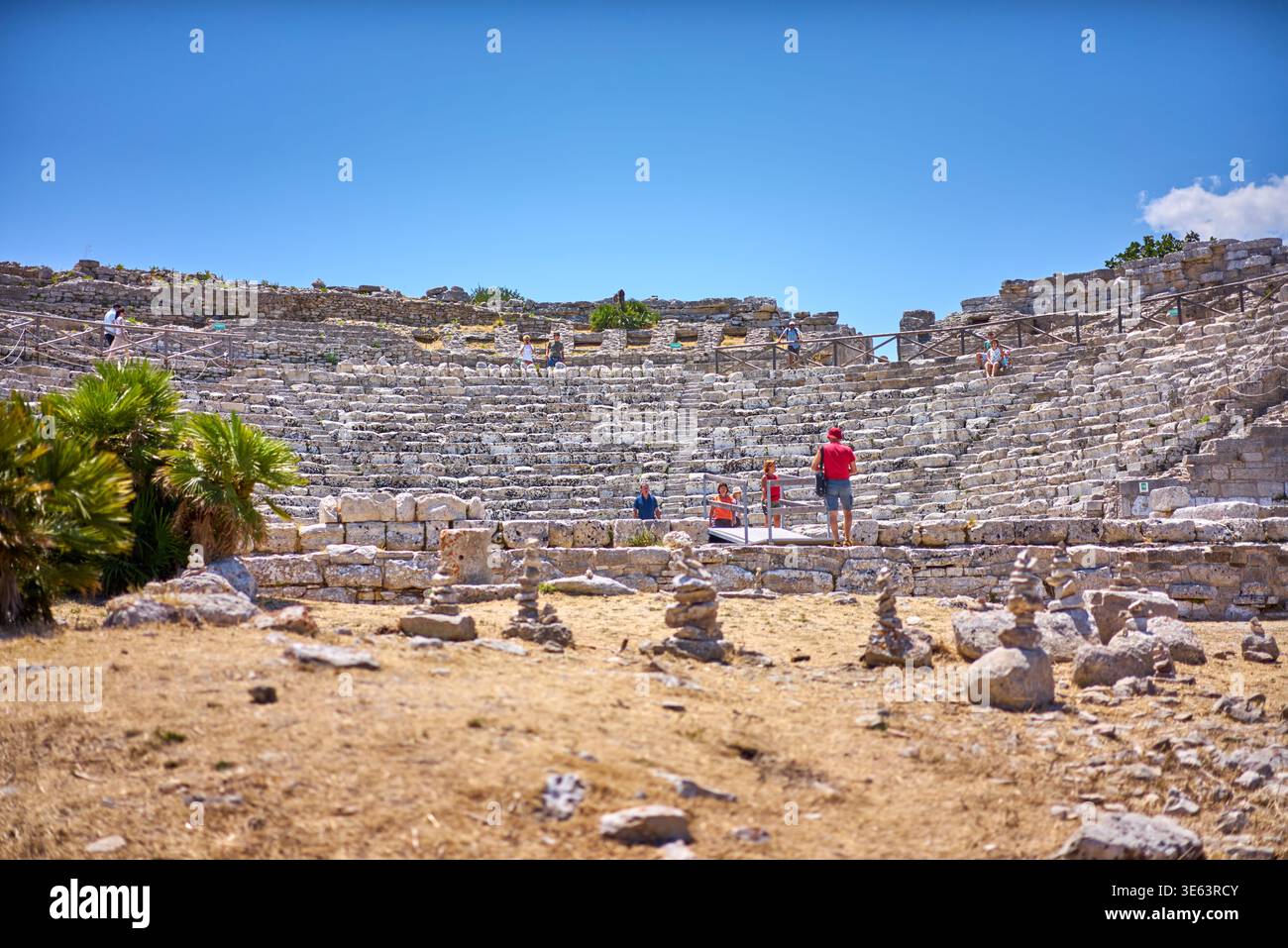 Antico anfiteatro in pietra con posti a sedere a più livelli disposti in uno schema semicircolare sotto un cielo azzurro. Le rovine calcaree sono caratterizzate dalle intemperie Foto Stock