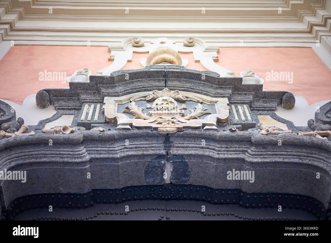 Dettaglio architettonico ravvicinato di un portale in pietra barocca con un rilievo centrale al cranio circondato da ornate scrollwork e ossa incrociate. L'oscurità Foto Stock
