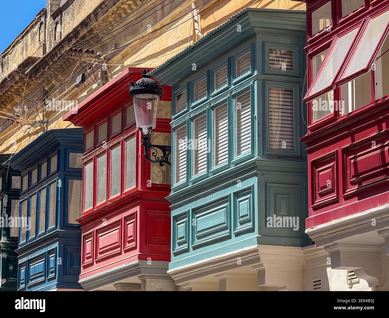 Primo piano di colorati balconi chiusi in legno (gallarija) su edifici in pietra calcarea a Rabat, Malta, con lampada da strada in ferro e cavi elettrici Foto Stock