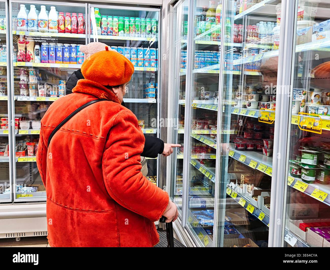 Kirov, Russia - 12 gennaio 2026: Due clienti si trovano di fronte a un frigorifero con sportello in vetro per controllare vari prodotti caseari e decidere cosa acquistare in un Foto Stock
