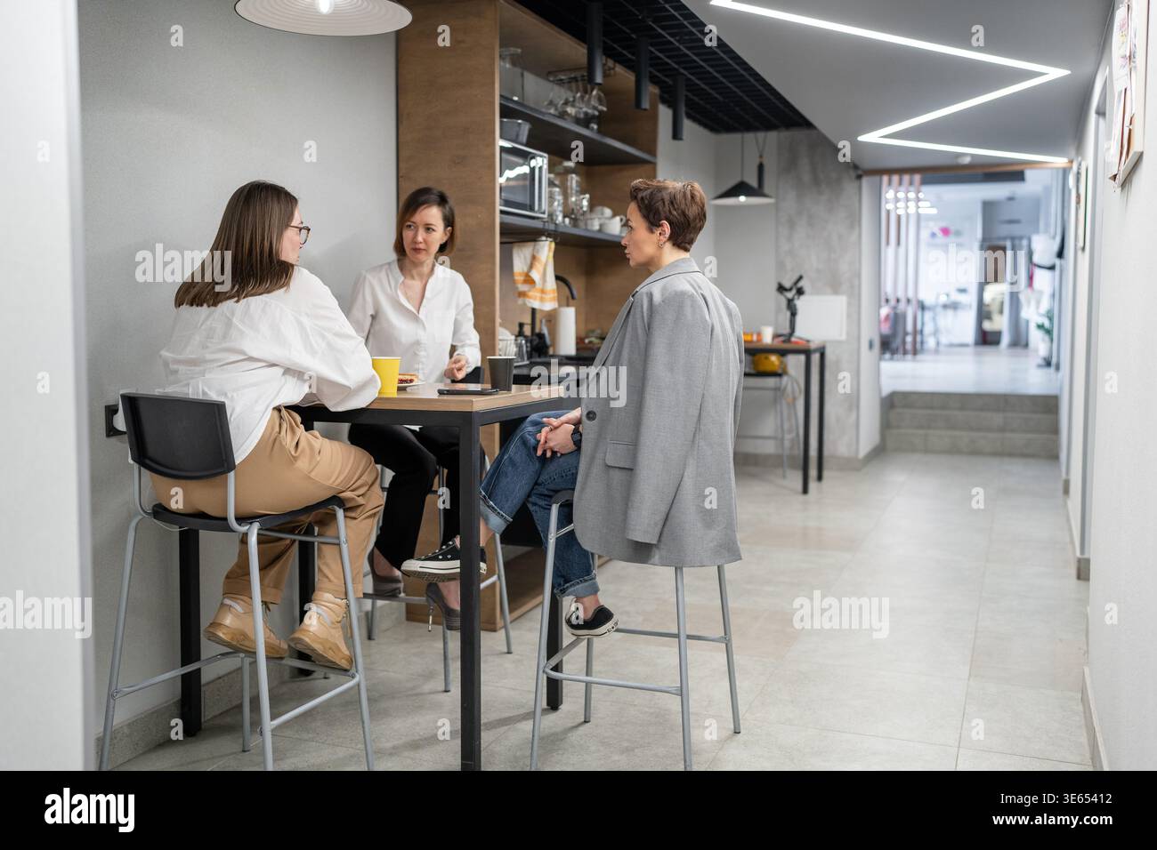 Due donne e una collega pranzano insieme al tavolo della cucina durante la pausa d'ufficio. Mangiare, pranzo, cucina, lavoro di squadra, tavolo alto, ufficio. Foto Stock