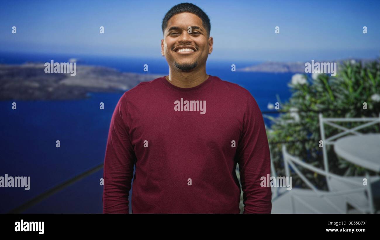 Uomo con barba sorridente, che mostra i denti e sta in piedi davanti a una terrazza dell'edificio; viaggio gioioso relax. Foto Stock