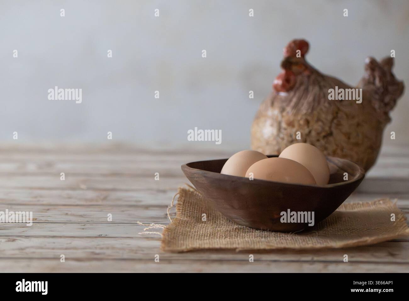 Uova marroni fresche in ciotola rustica di legno con gallina in ceramica su legno in legno invecchiato con spazio per copie Foto Stock