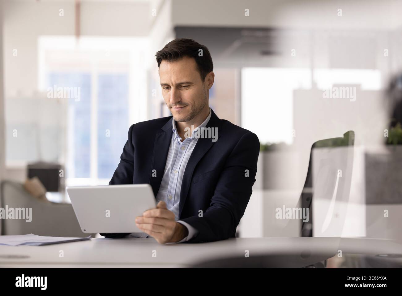 Uomo d'affari ispanico adulto che esamina documenti utilizzando un tablet in ufficio Foto Stock