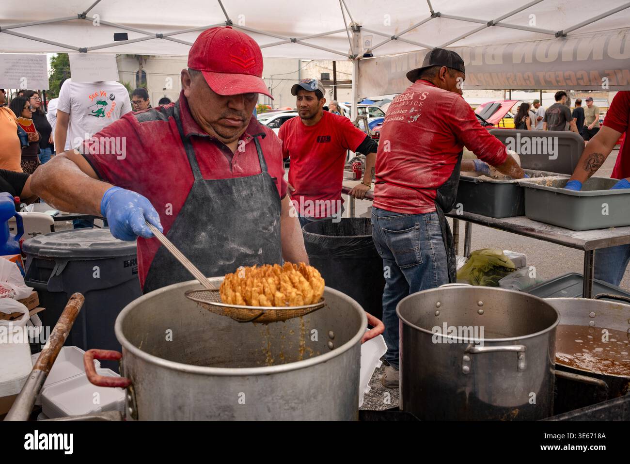 Cook trattiene cipolla fritta a fette, cipolla Bloomin, da un recipiente di olio caldo, friggitrice, al Texas Onion Fest, Weslaco, Texas, USA. SOLO PER USO EDITORIALE Foto Stock