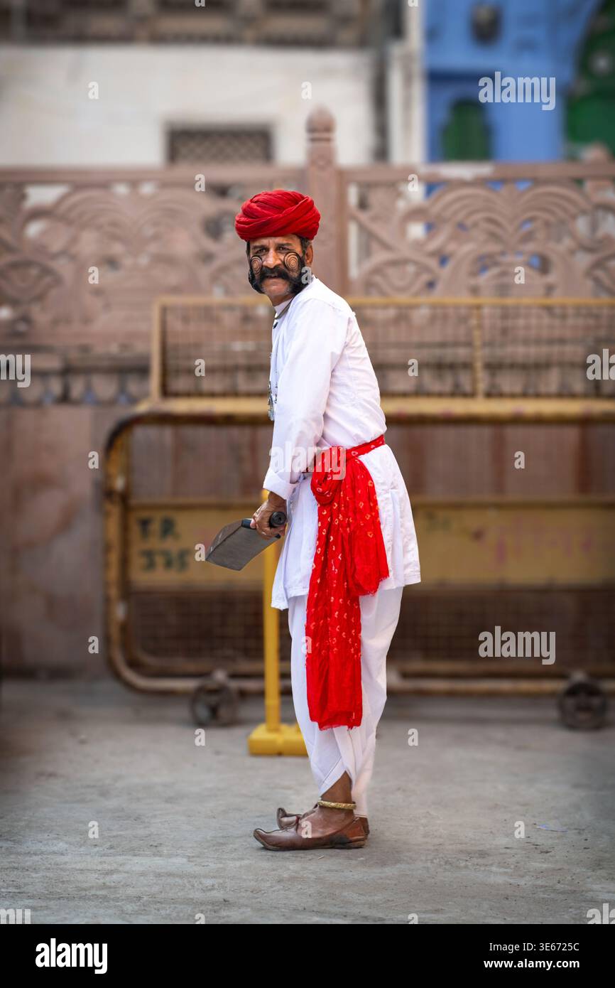 Un uomo del Rajasthan con baffi e un turbante rosso che gioca a cricket in strada a Jodhpur, in India Foto Stock