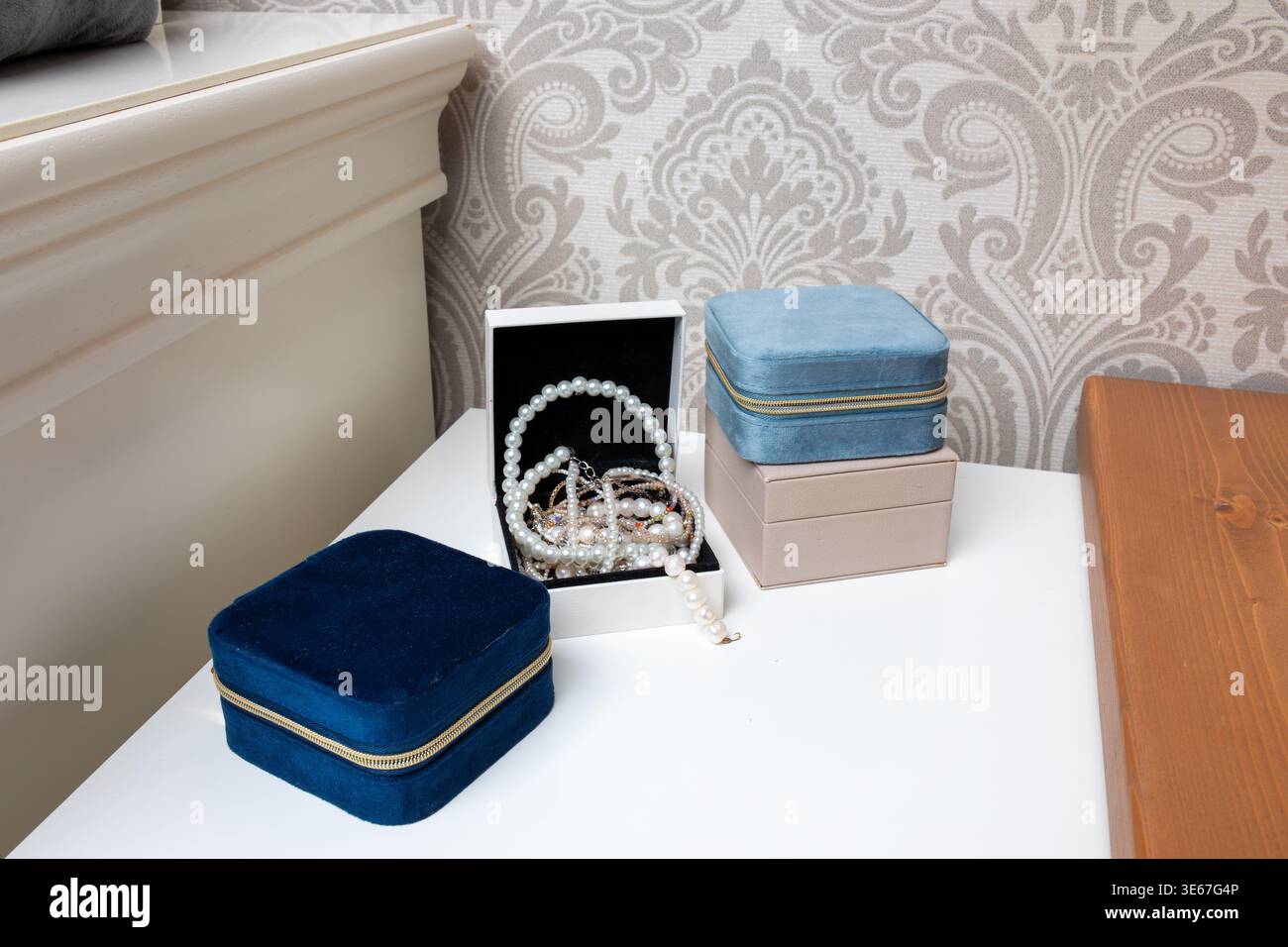 Gruppo di gioielli in velluto di vari colori, tra cui blu, beige e azzurro su un tavolo da toeletta bianco con una collana di perle all'interno Foto Stock