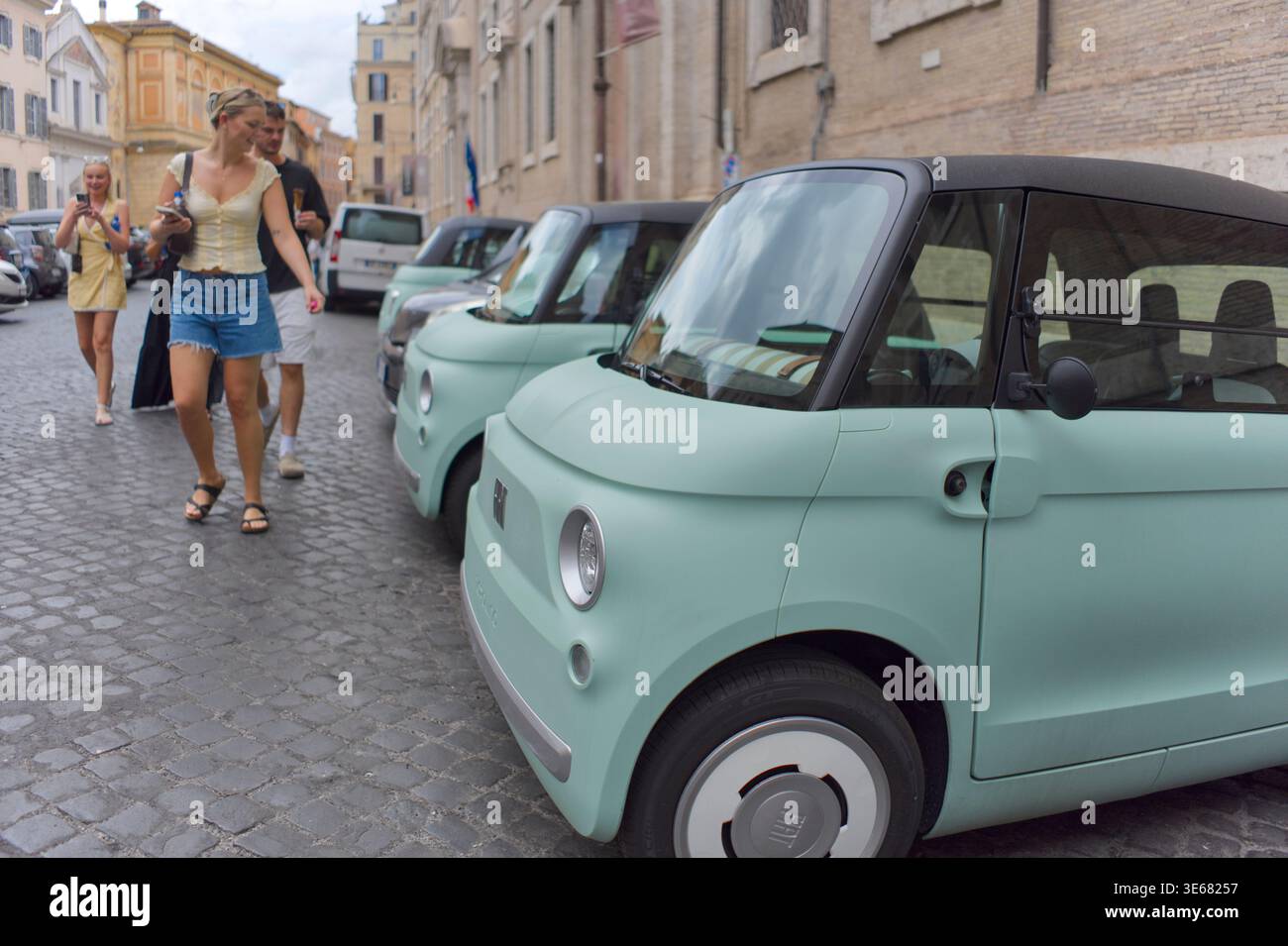 le auto elettriche fiat topolino parcheggiate in via centro storico sono di colore verde uovo che i turisti li guardano Foto Stock