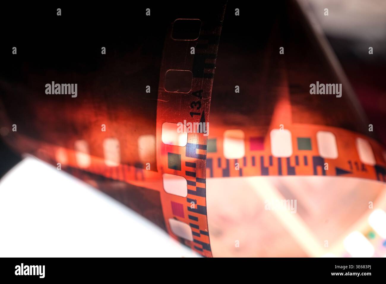 Primo piano di strisce di pellicola fotografica arricciate da 35 mm con tonalità arancione-rosse e fori del pignone, retroilluminati per un look astratto Foto Stock