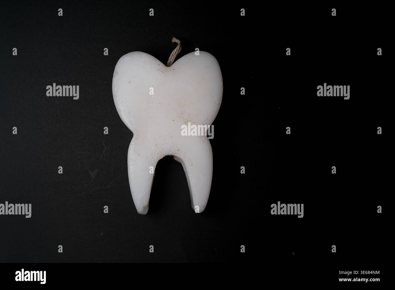 Candela bianca a forma di dente con stoppino su sfondo nero scuro, composizione minima, vista dall'alto verso il basso, oggetto isolato Foto Stock