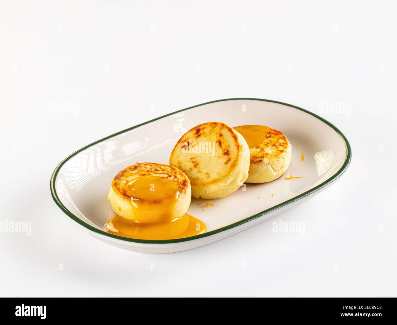 Uno shot minimalista di tre sirniki dorati, o frittelle di formaggio, condite con salsa gialla brillante. Servita su un piatto e isolata su una cle Foto Stock