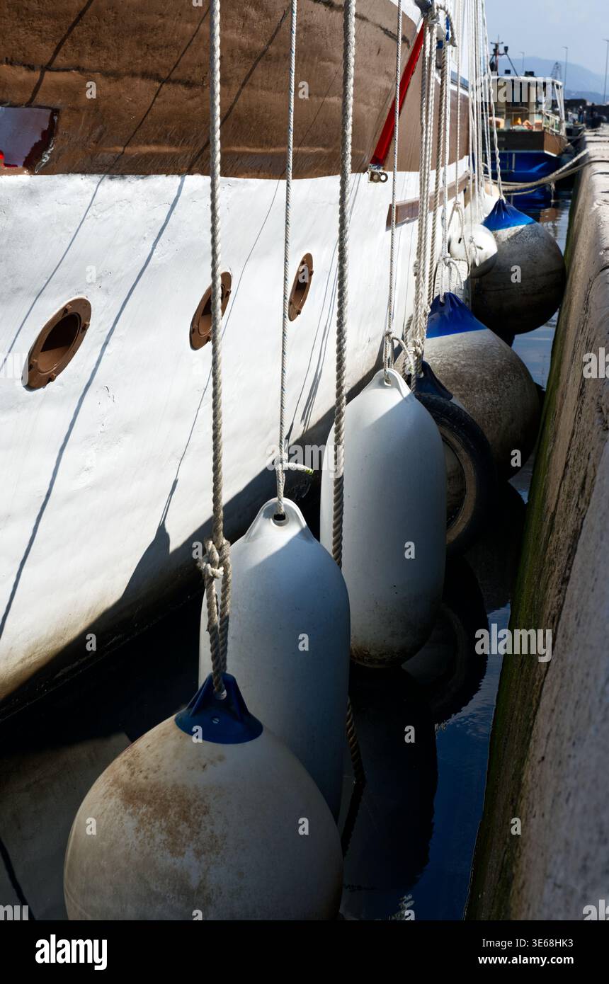 Vista ravvicinata dei paraurti del parafango appesi lungo il lato di un'imbarcazione attraccata. La scena mette in evidenza le attrezzature di sicurezza nautica, le corde, i dettagli dello scafo, Foto Stock