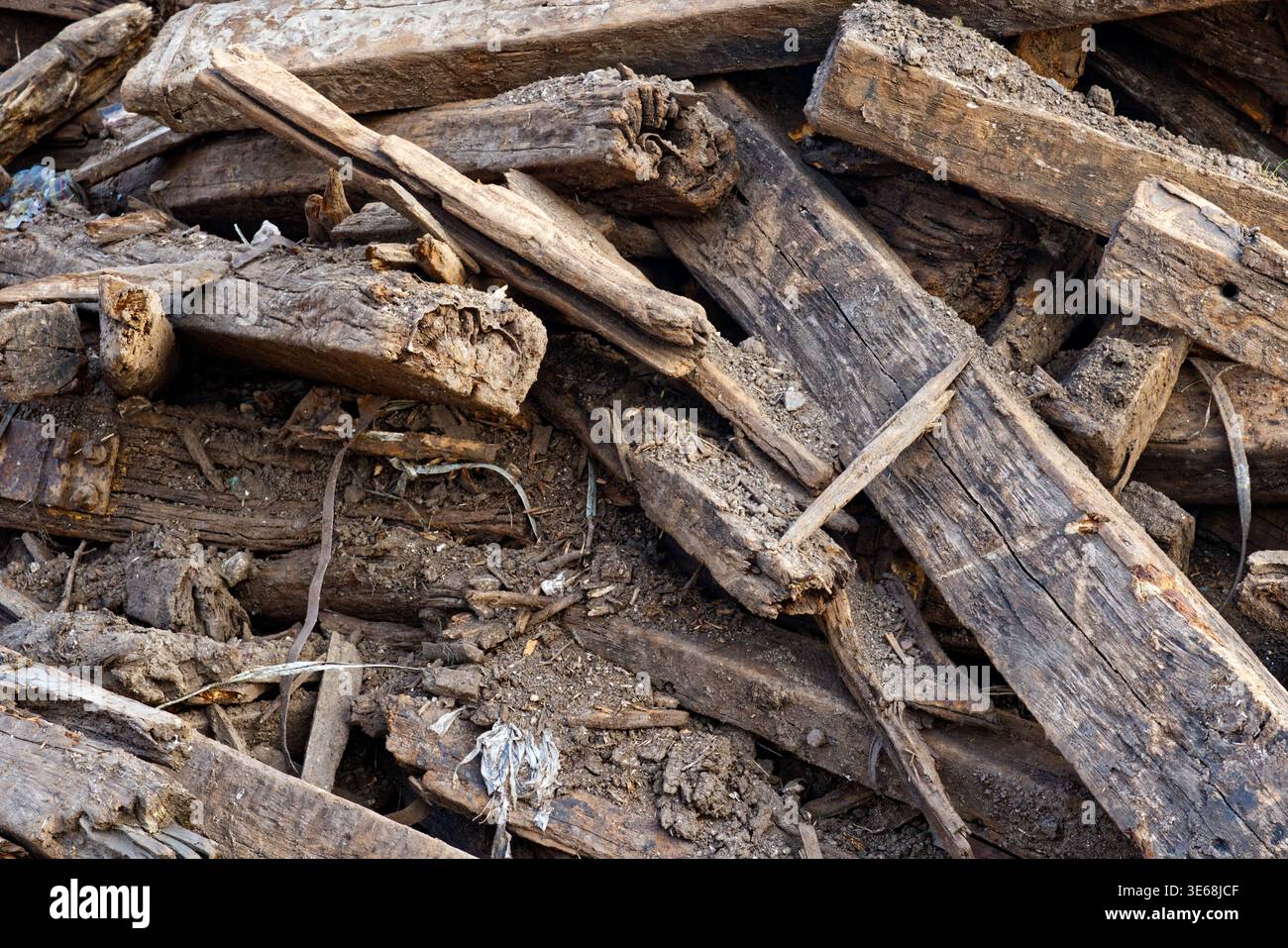 Una vista dettagliata dall'alto verso il basso di un mucchio di traverse in legno scartate, in decomposizione, mescolate con terreno e detriti industriali. Il legno mostra segni pesanti Foto Stock