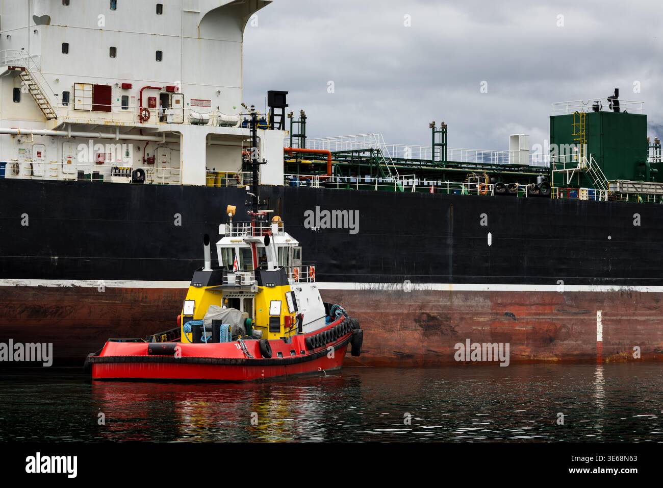 Piccolo rimorchiatore che si muove accanto a una grande cisterna merci nel porto. Settore marittimo industriale che presenta logistica di spedizione, operazioni portuali e mari Foto Stock