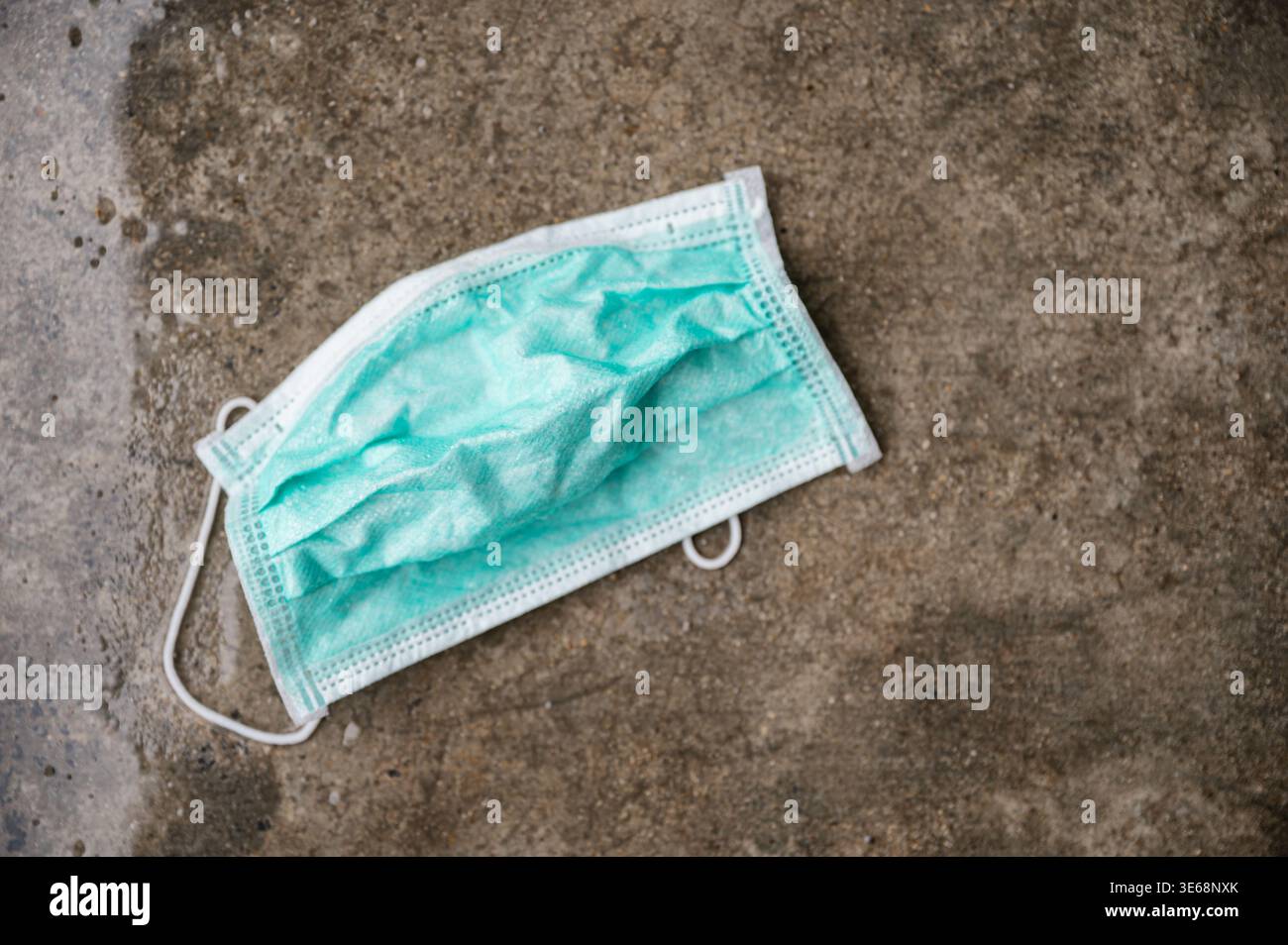 Sporco bagnato maschera medica lasciare su pavimento di cemento Foto Stock
