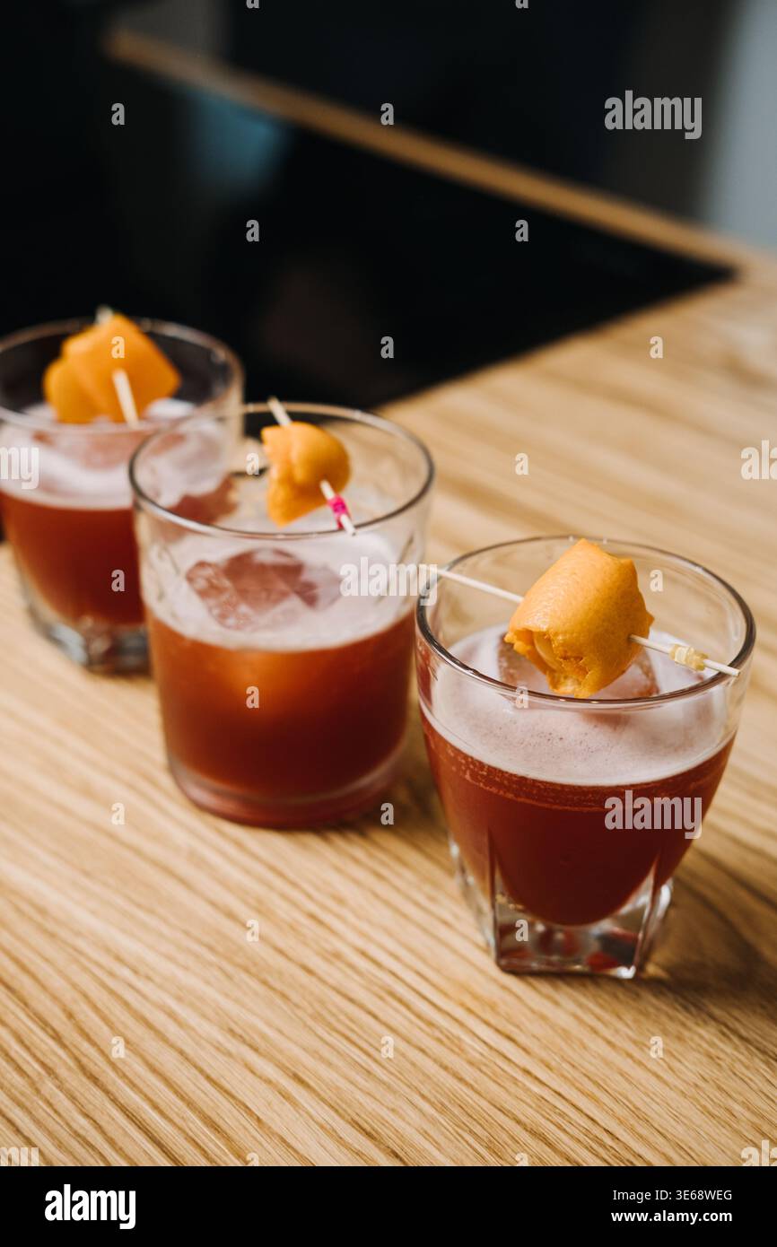 Tre bevande rosse guarnite con bucce d'arancia siedono su un tavolo di legno. Bere consapevole della salute, rituale senza alcol, celebrazione consapevole. Foto Stock