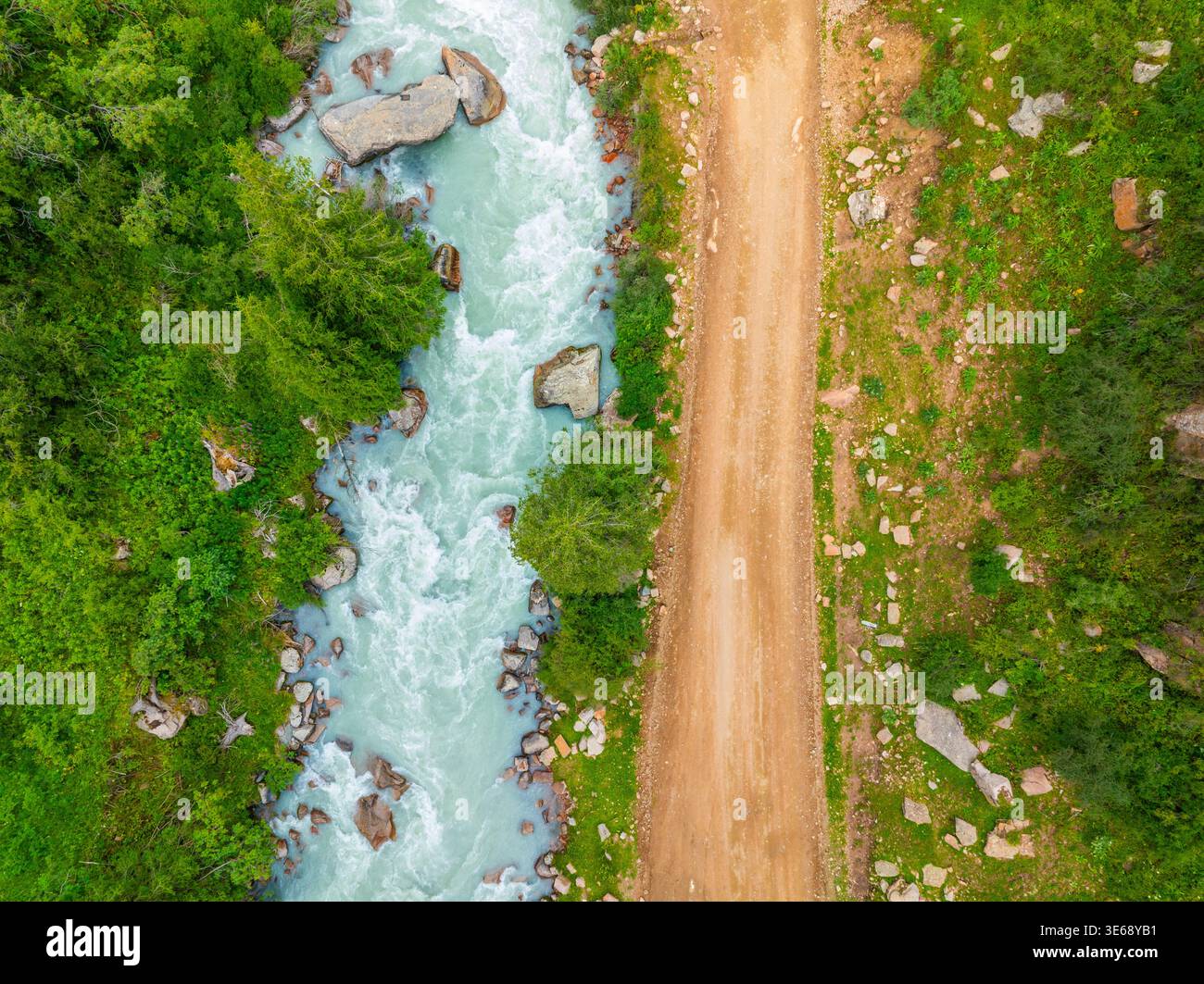 Il tranquillo fiume di montagna scorre lungo la strada sterrata non asfaltata in Kirghizistan. Alberi lussureggianti e rocce impreziosiscono il tranquillo paesaggio naturale durante il giorno. Dir Foto Stock