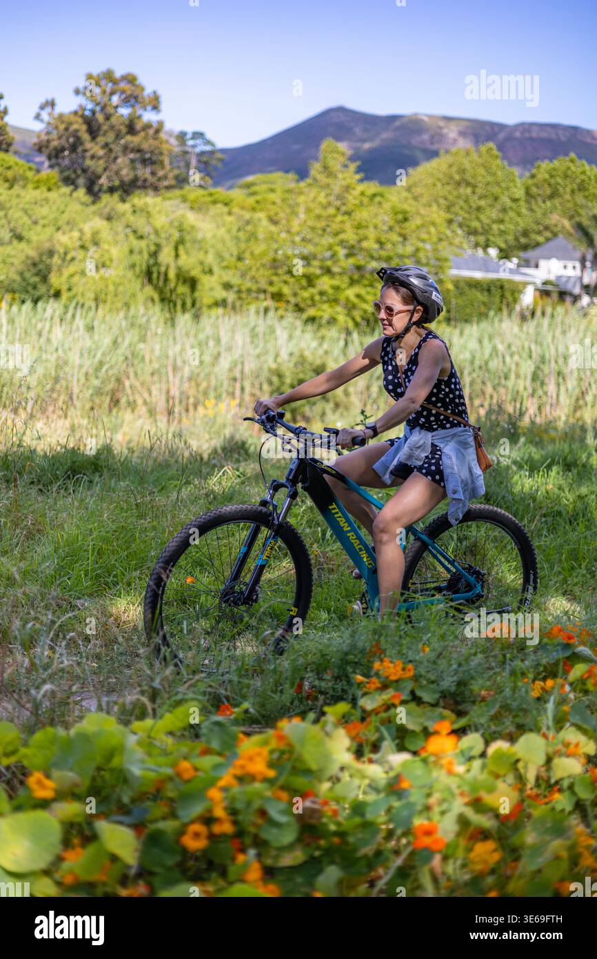 Donna in bicicletta lungo una delle cinture verdi di Città del Capo con nasturzi in primo piano e la Montagna della Tavola sullo sfondo, durante una vittoria di Bike-and-Hike Foto Stock