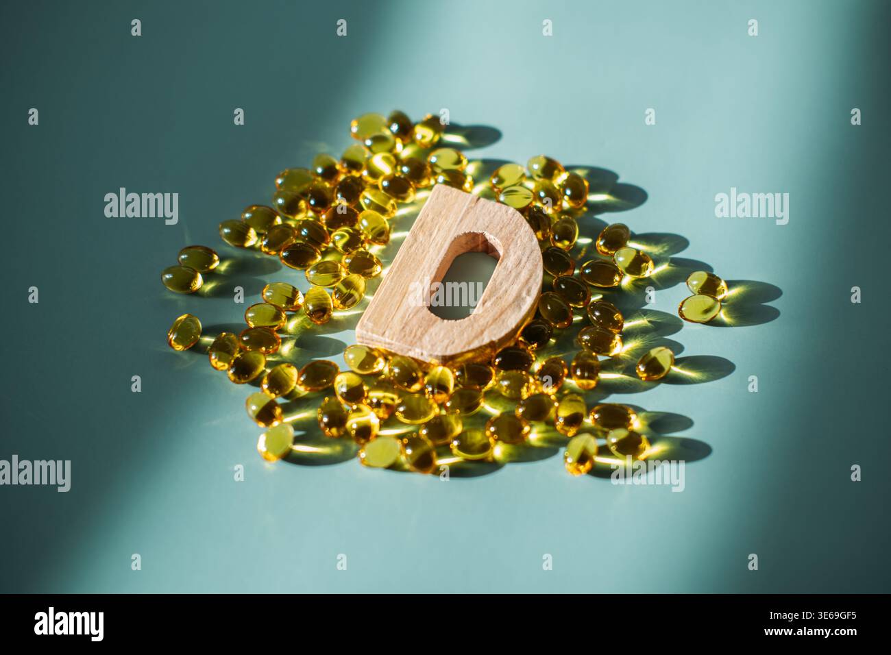 La piccola lettera di legno D si trova tra le capsule gialle degli integratori traslucidi sulla superficie blu. Carenza di vitamina D, supporto del sistema immunitario, preventivo Foto Stock