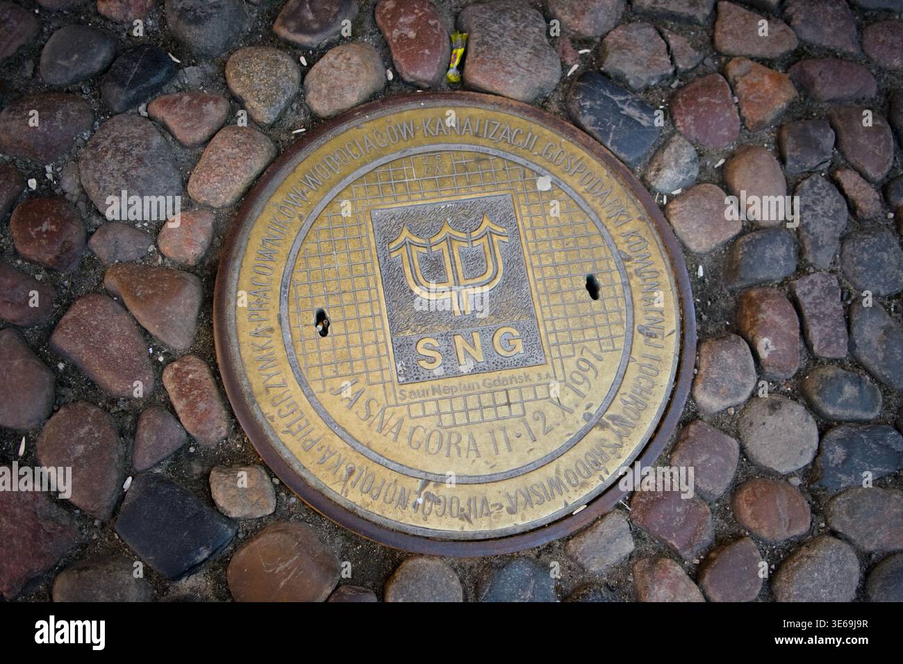 Tombino decorativo di Saur Neptun Gdańsk water utility con logo tridente su ciottoli, Polonia Foto Stock