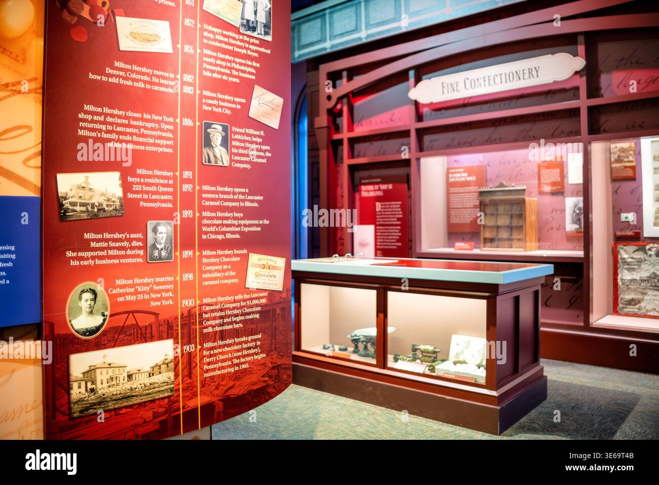 Esposizione cronologica del Museo Hershey Story Hershey Stati Uniti | HERSHEY, Pennsylvania — Un pannello espositivo cronologico e una vetrina di "Fine Confectionery" delineano la storia imprenditoriale iniziale di Milton S. Hershey all'interno del Museo Hershey Story. La linea del tempo evidenzia i primi fallimenti commerciali di Hershey prima del suo grande successo con la fondazione della Lancaster Caramel Company nel 1886. Artefatti accompagnatori, come stampi e bilance d'epoca, contestualizzano la sua decisione fondamentale del 1893 di acquistare attrezzature per la produzione di cioccolato alla Fiera Colombiana del Mondo. Questa scelta strategica Foto Stock