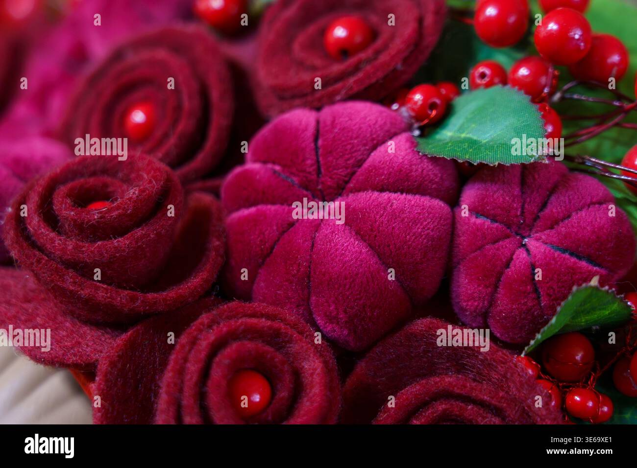 Fiori di feltro colorati e frutti di bosco rossi in una disposizione decorativa esposta Foto Stock