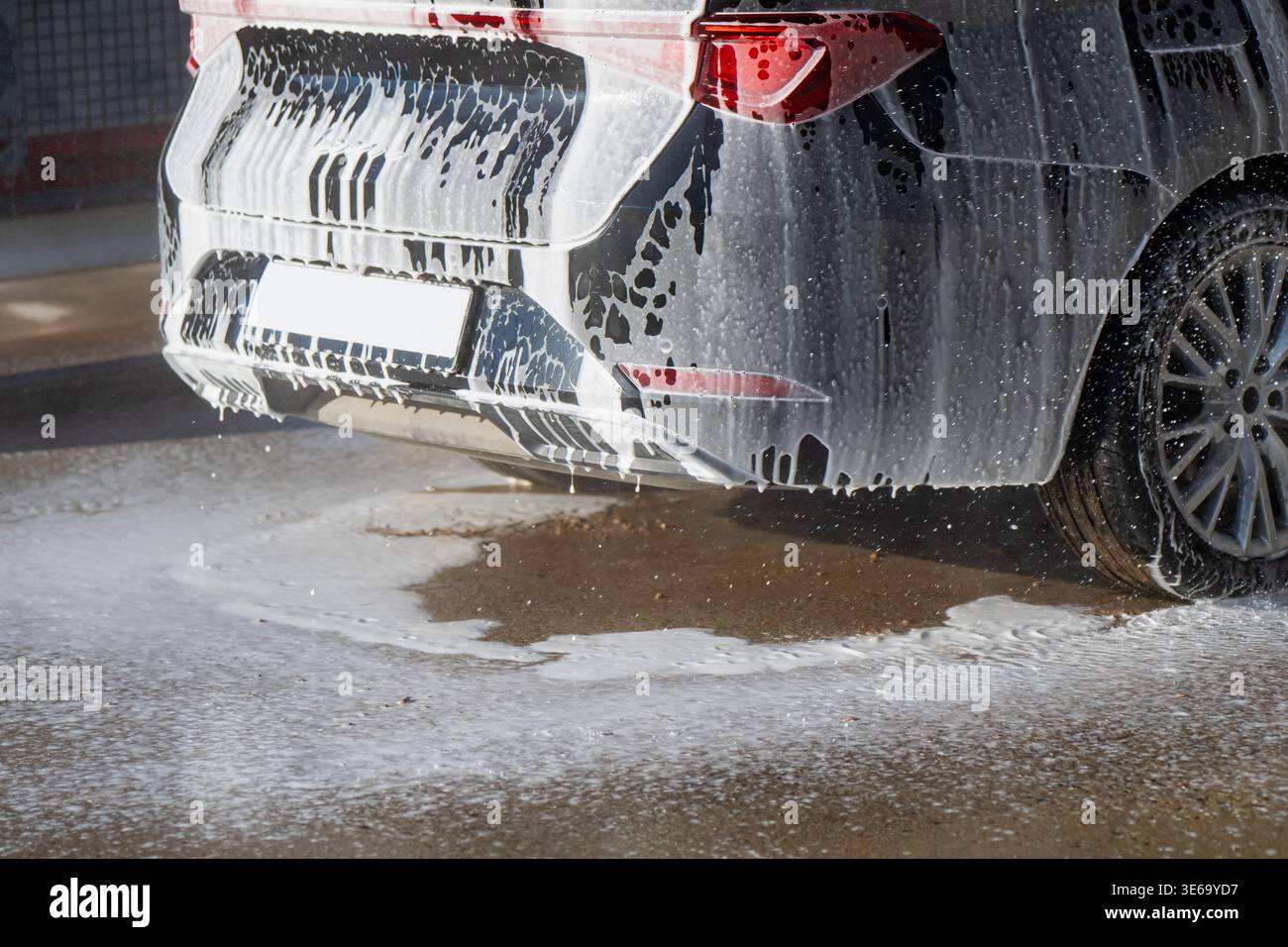 Parte posteriore del SUV coperto di sapone durante il lavaggio self-service, che riflette la manutenzione automobilistica, le abitudini e le tendenze di cura dei veicoli di consumo Foto Stock