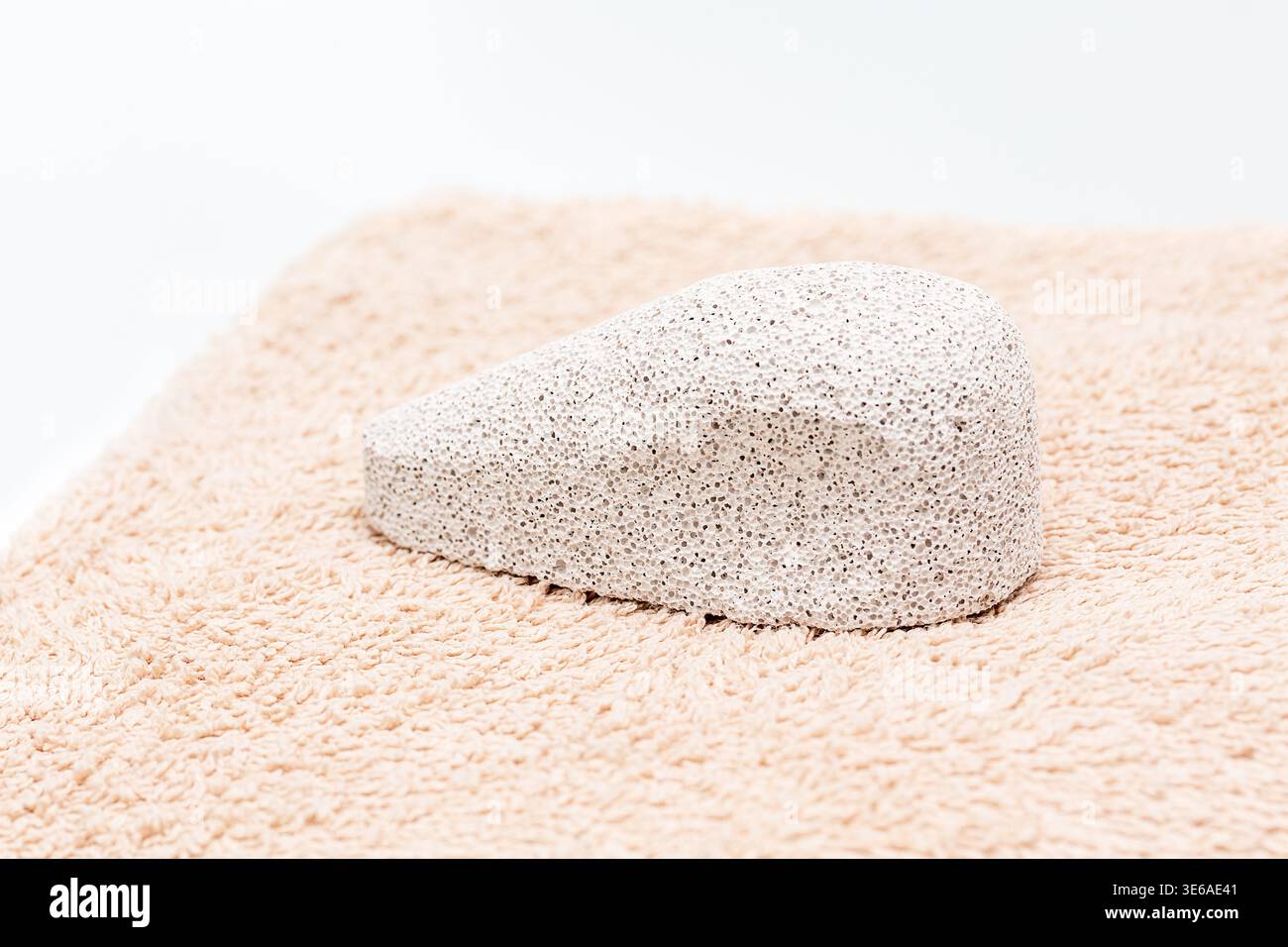 Pietra pomice bianca posta su un morbido asciugamano beige, che mostra la sua consistenza porosa e la sua forma unica, ideale per la cura personale e le routine di bellezza Foto Stock