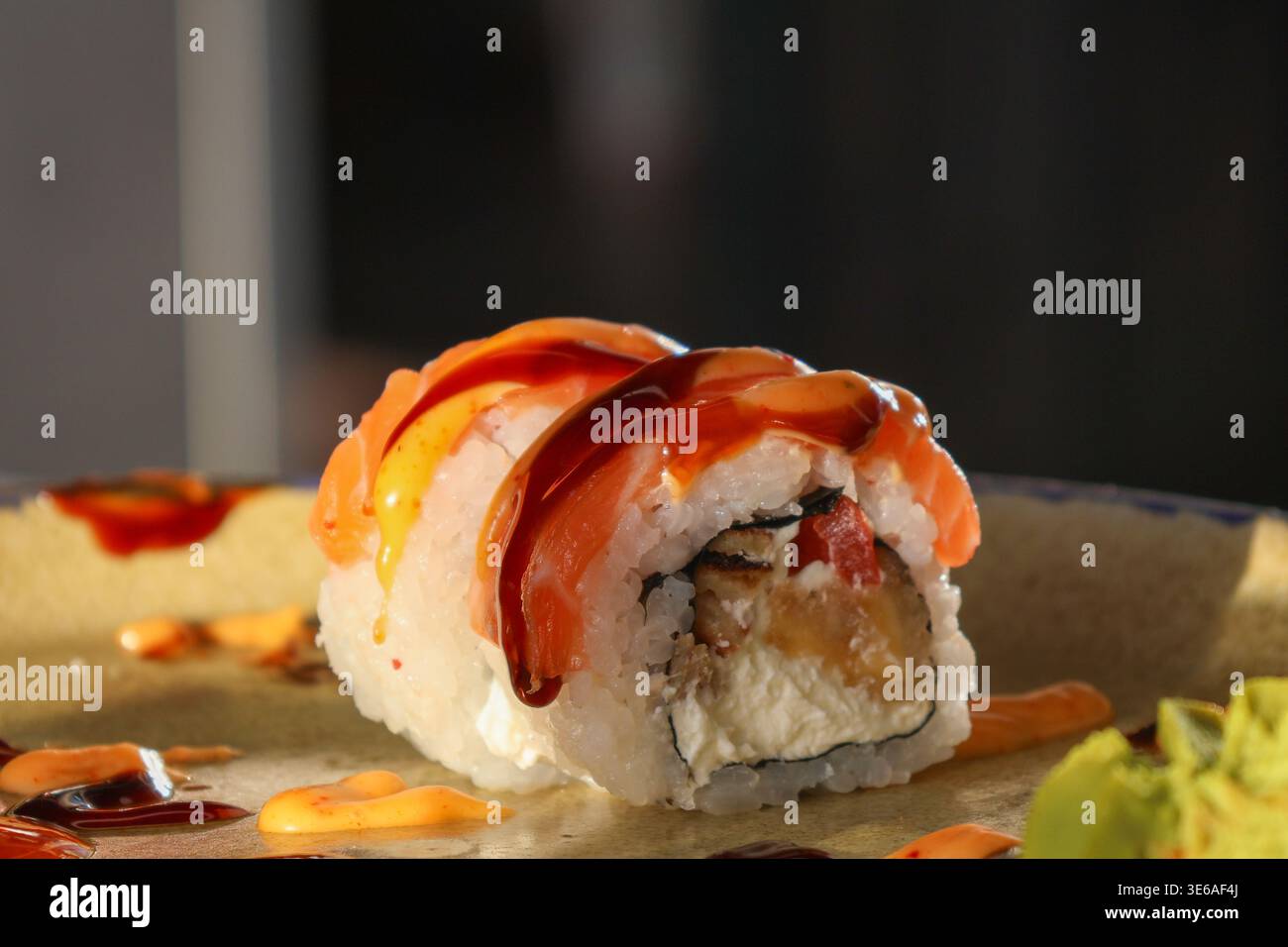Un sushi roll si appoggia su un piatto con la salsa versata sopra e il wasabi accanto. L'ambiente e' un ristorante durante un pasto con vari condimenti. Foto Stock