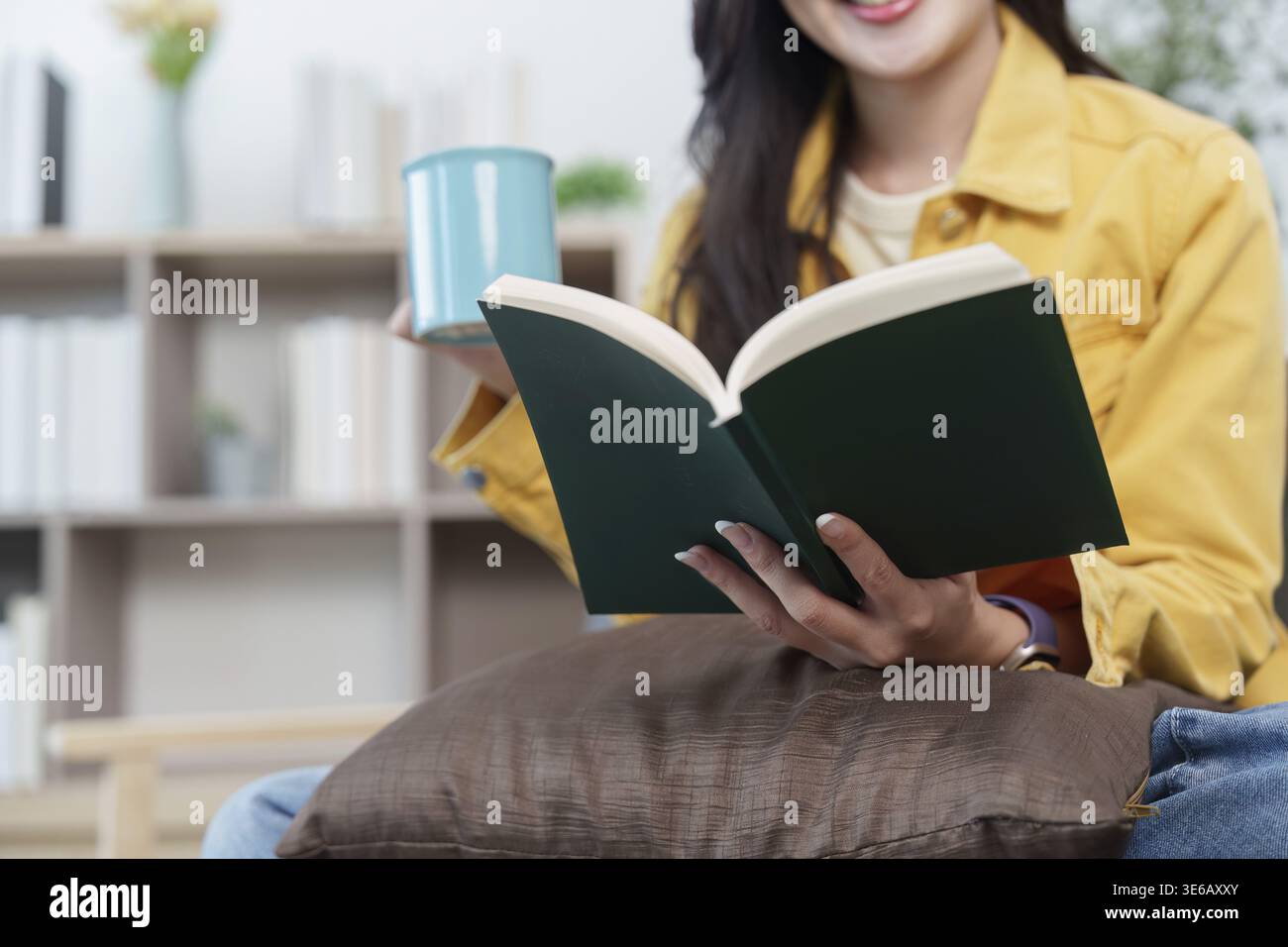 Una giovane donna ama leggere un libro e sorseggiare un caffè, mostrando uno stile di vita di relax e piacere personale Foto Stock