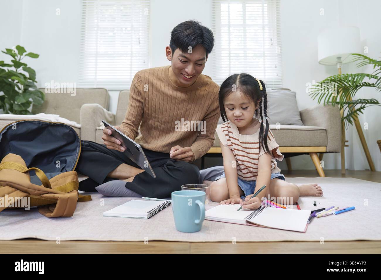 Padre e figlia si godono una sessione di studio creativa, circondati da materiale scolastico nel loro invitante spazio abitativo Foto Stock