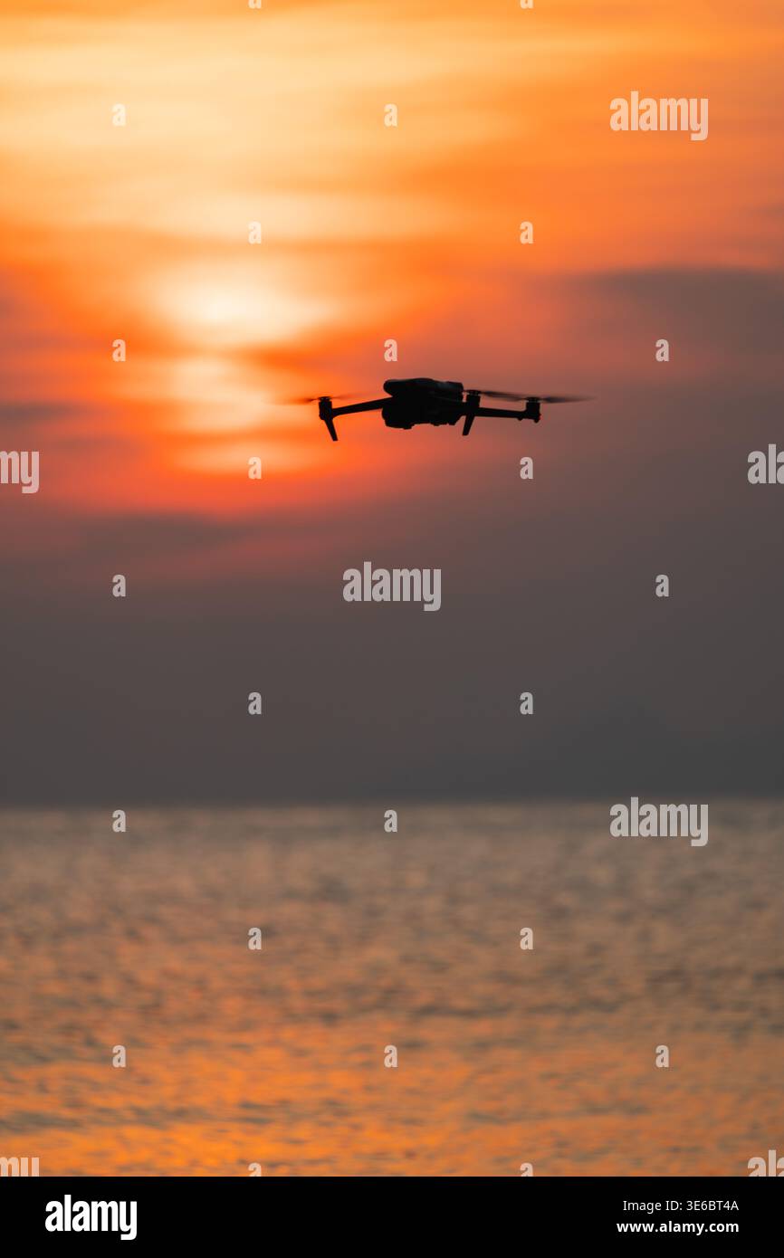 Drone che vola sul mare al tramonto con un cielo spettacolare, concetto di veicolo aereo senza equipaggio Foto Stock