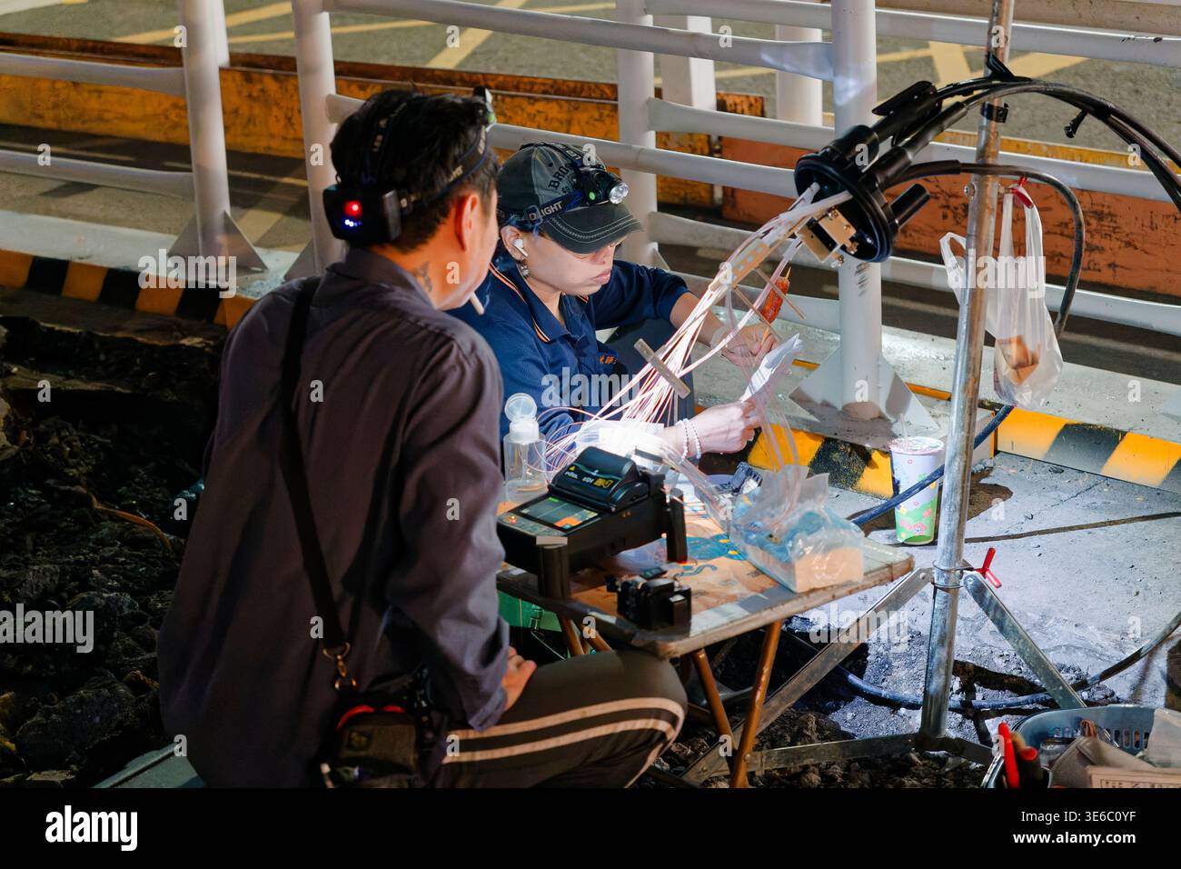Taipei, Taiwan - 19 ottobre 2024: I tecnici eseguono la giunzione di fusione a fibre ottiche su un marciapiede di notte, utilizzando l'attrezzatura sotto i fari. Foto Stock