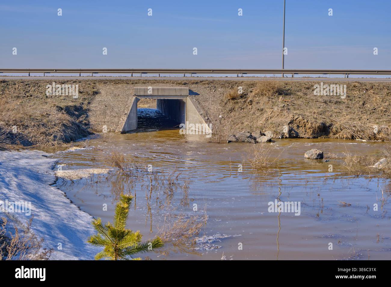 Alto livello dell'acqua vicino alla strada autostradale durante lo scongelamento primaverile, mostrando le infrastrutture e i cambiamenti stagionali della natura Foto Stock