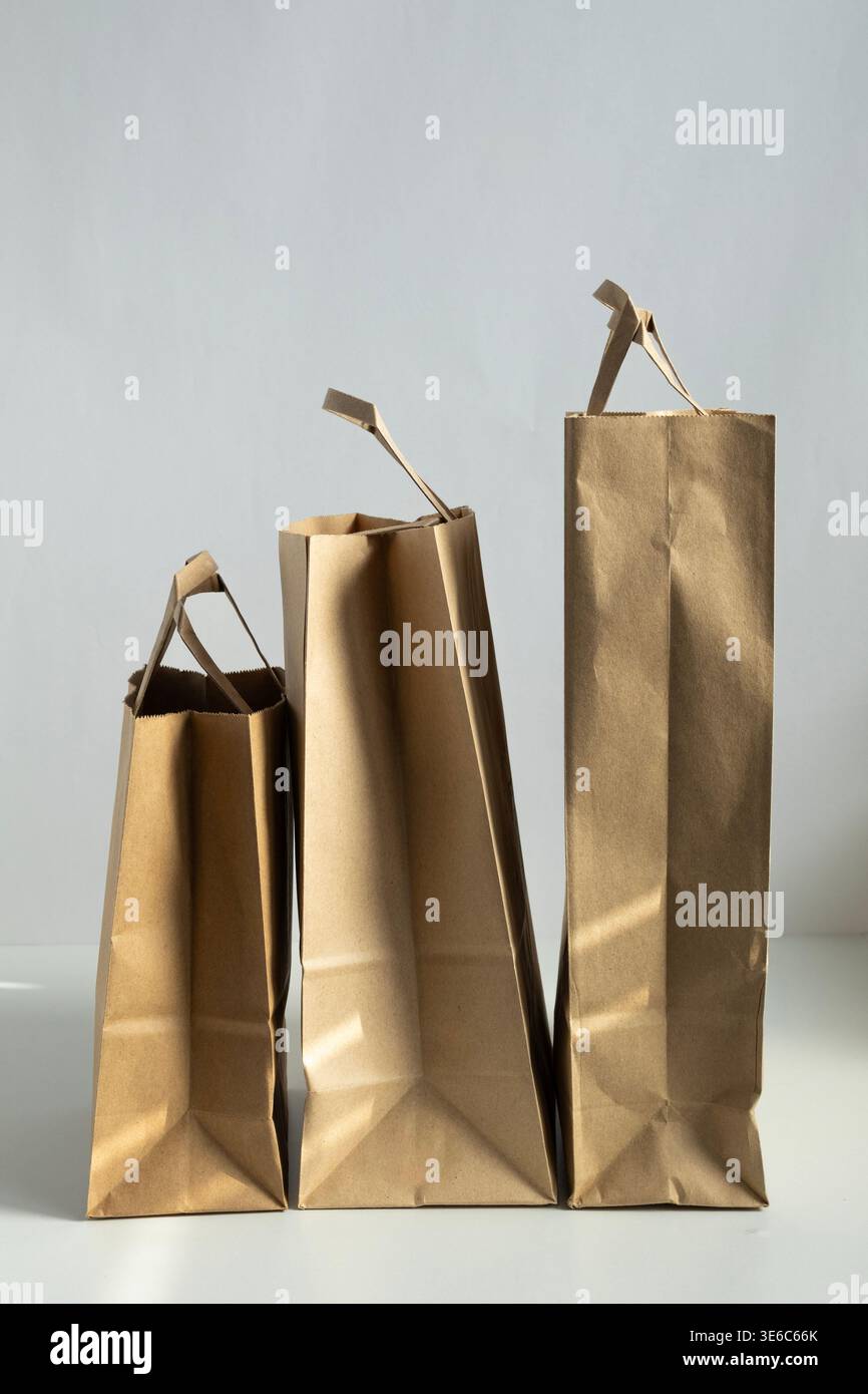 Composizione minimale di borse della spesa in carta kraft su sfondo chiaro con luce naturale e ombre. Concetto di imballaggio ecologico per la vendita al dettaglio Foto Stock