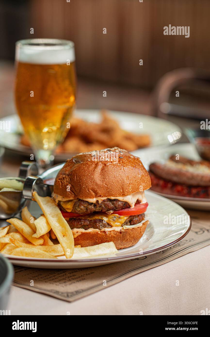 Cheeseburger con patatine fritte e birra in tavola Foto Stock