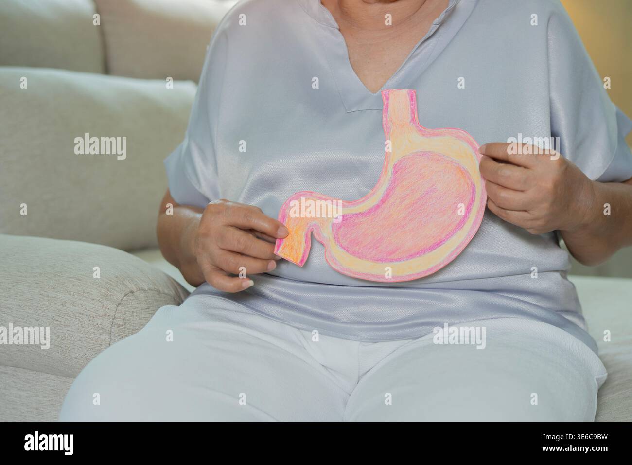 Donna anziana seduta sul divano e che tiene l'organo dello stomaco fatto di carta. Concetto di screening del cancro gastrico, trapianto di stomaco, probl. Del tratto digerente Foto Stock