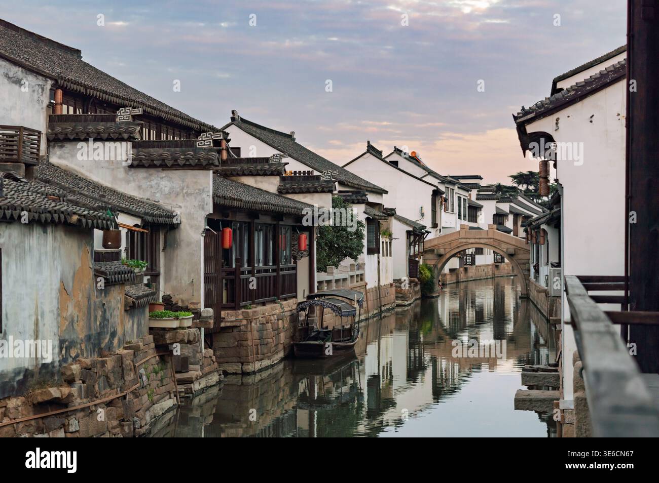 La storica architettura cinese della città sull'acqua incornicia un tranquillo canale con un classico ponte di pietra sotto un morbido cielo mattutino Foto Stock