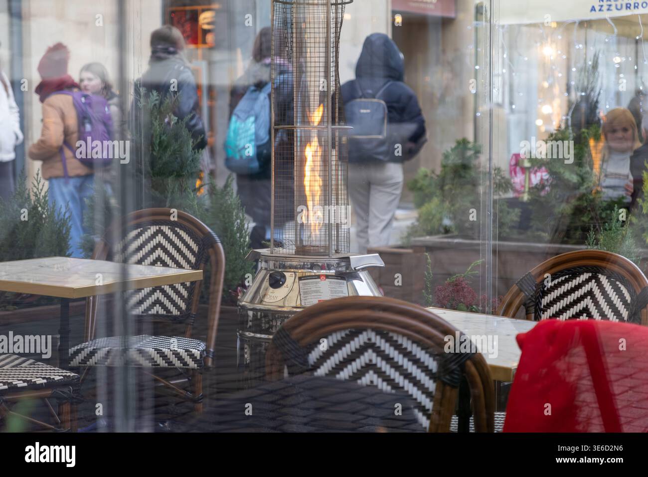 Vista interna dell'area pranzo all'aperto della caffetteria urbana, dotata di un caldo patio riscaldato, comodi posti a sedere e riflessi di vetro dell'attività stradale, il che suggerisce un ambiente fresco Foto Stock
