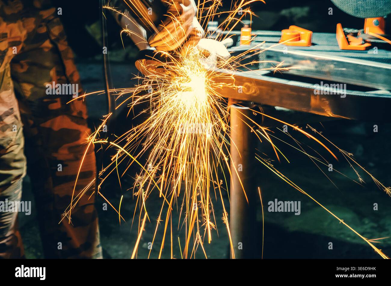 Scintille dorate derivanti dalla lucidatura dei metalli in officina. L'illuminazione intensa e lo sfondo scuro sfocato enfatizzano l'energia, il movimento e l'atmosfera industriale. Foto Stock