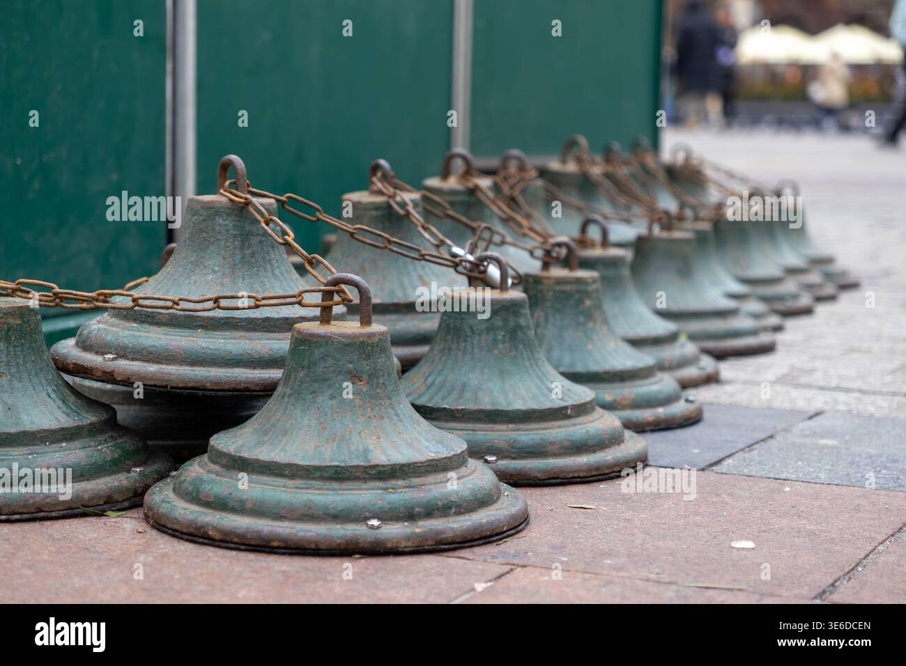 Vista ravvicinata dei pali di barriera in metallo verde a forma di campana collegati da catene ossidate, che definiscono l'accesso in una piazza storica della città o in un luogo pubblico più frequentato Foto Stock
