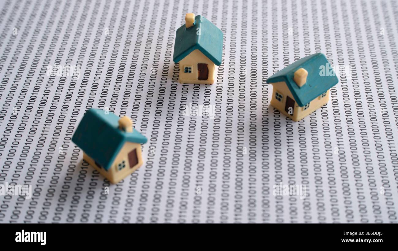 Piccole case in miniatura posizionate in cima a fogli di dati di codice binario, che rappresentano le tendenze del settore immobiliare digitale e della tecnologia immobiliare. Foto Stock