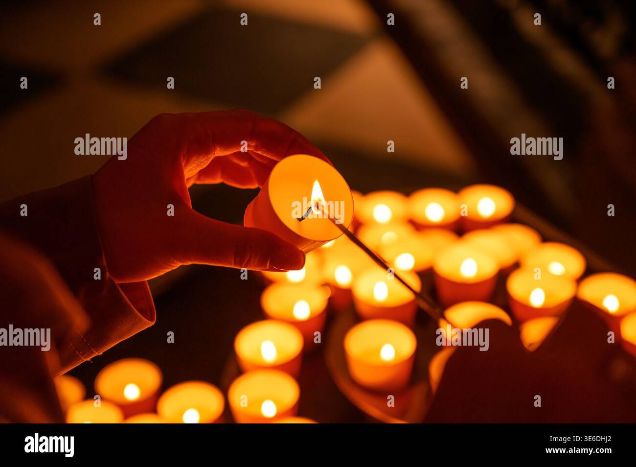 Accendere una piccola candela con un fiammifero in una stanza piena di luci da tè Foto Stock