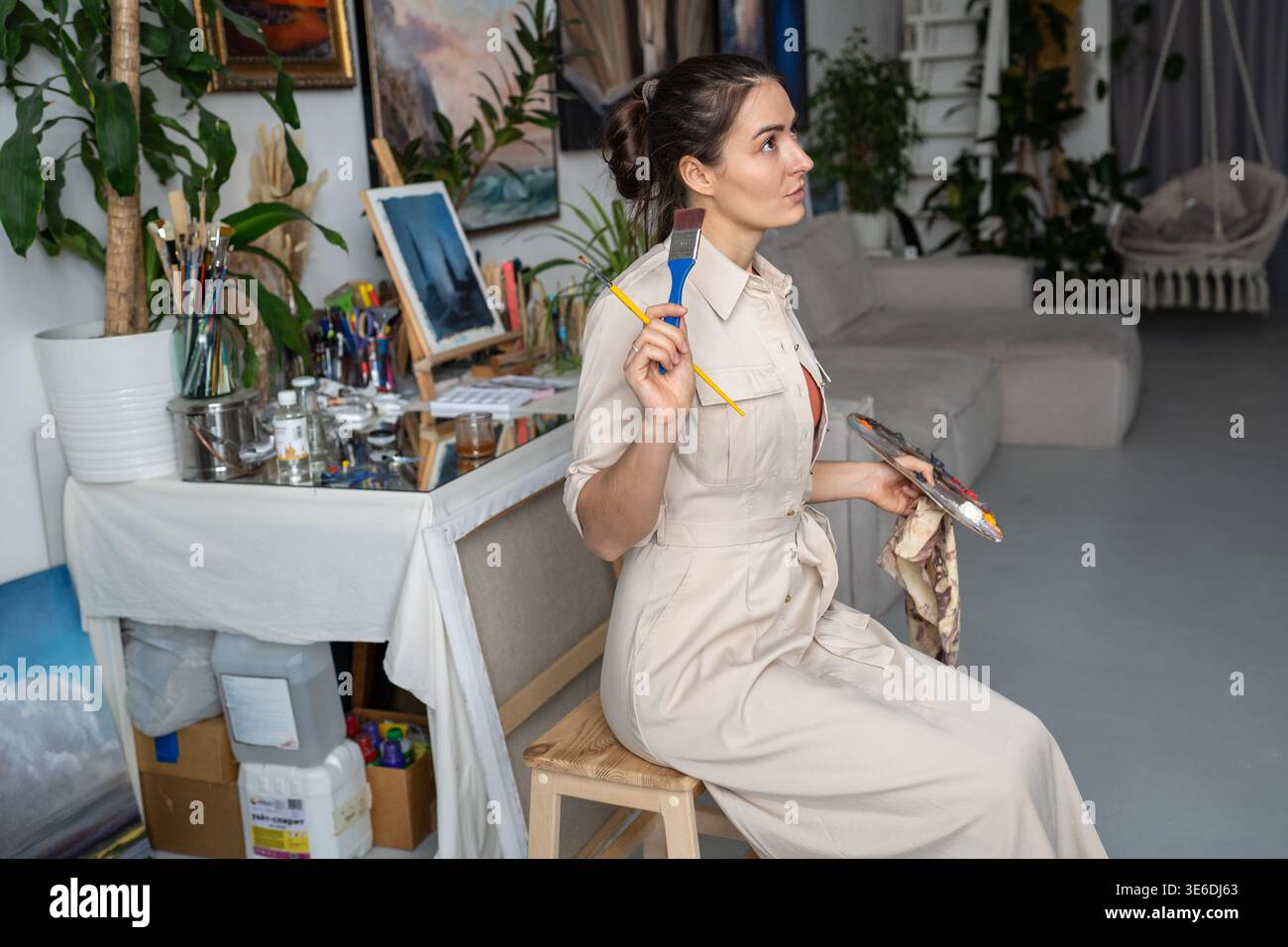 Donna abile designer artista in fase di creazione di opere d'arte, seduta a guardare dipingere su cavalletto. Foto Stock