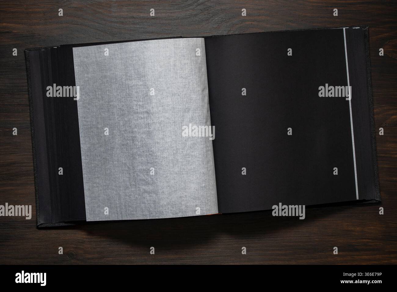 Apri album fotografico nero con una pagina testurizzata vuota su un tavolo di legno scuro, composizione minima con spazio di copia per design, memoria, scrapbooking o pres Foto Stock