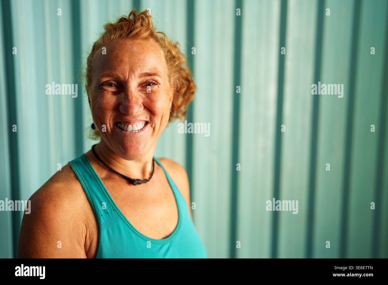 Una donna con un sorriso allegro, lentiggini e capelli ricci sta trasmettendo dopo una sessione di allenamento. La sua espressione gioiosa riflette l'impegno a rimanere in salute Foto Stock
