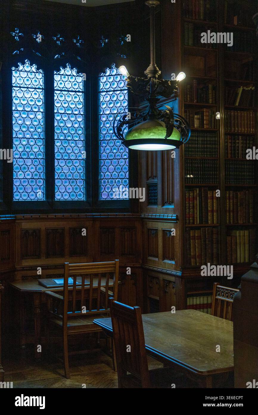 Un'alcova di lettura nella John Rylands Library, Manchester, con finestre con piombo a occhio di bue, lampada a sospensione e scaffali in quercia scura. Foto Stock