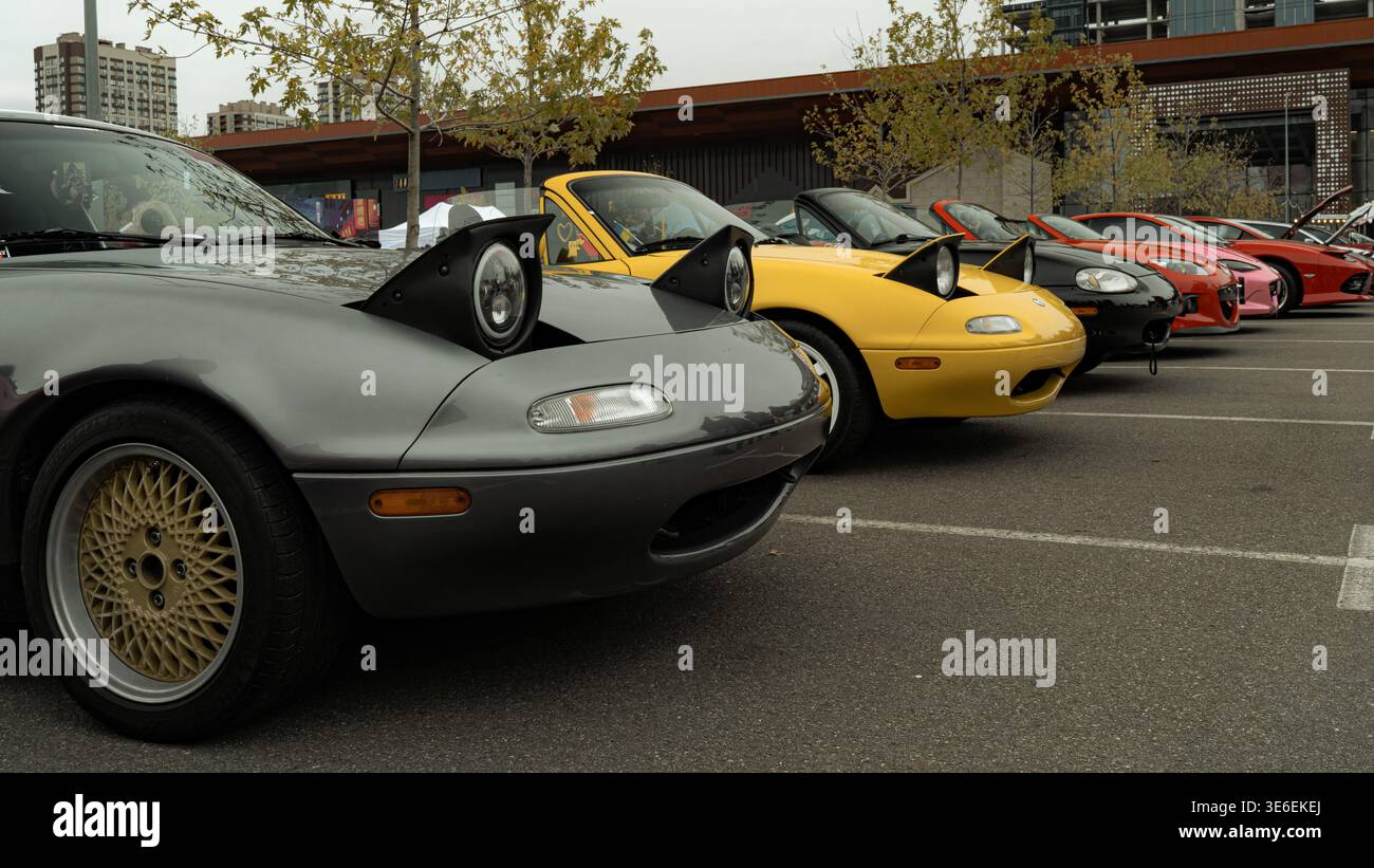 Linea di roadster Mazda MX-5 con fari a scomparsa rialzati parcheggiati all'aperto in occasione di un festival automobilistico. Auto sportive colorate fotografate in una città Foto Stock